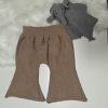 Amandas Babystrik-kollektion byder på brune strikkede babybukser på en hvid overflade ved siden af et gråt Kopier-elefantlegetøj med en blød hvid stofbagtæppe for ekstra hygge.