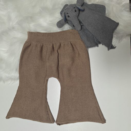 Amandas Babystrik-kollektion byder på brune strikkede babybukser på en hvid overflade ved siden af et gråt Kopier-elefantlegetøj med en blød hvid stofbagtæppe for ekstra hygge.